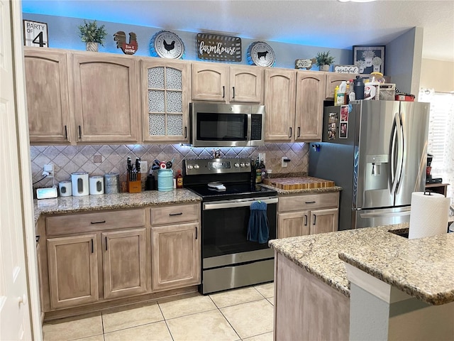 kitchen with decorative backsplash, light tile patterned floors, light stone countertops, light brown cabinetry, and appliances with stainless steel finishes