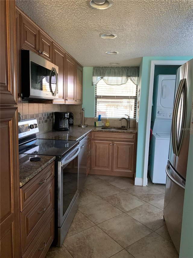 kitchen with tasteful backsplash, stainless steel appliances, sink, stacked washer and clothes dryer, and light tile patterned flooring