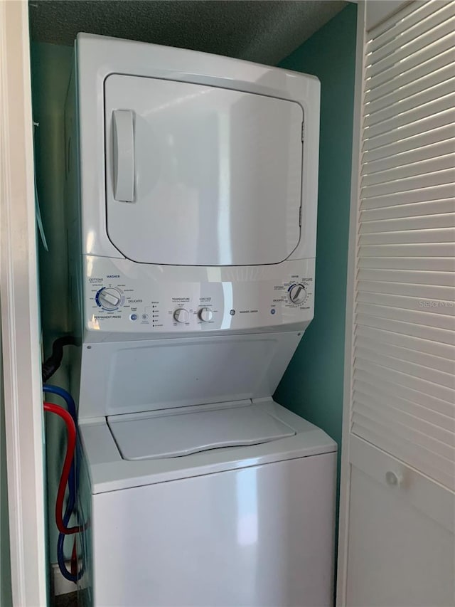 clothes washing area featuring a textured ceiling and stacked washer / drying machine