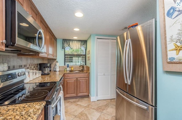 kitchen with sink, light stone counters, a textured ceiling, decorative backsplash, and appliances with stainless steel finishes