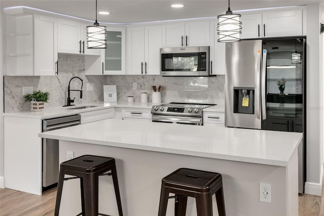 kitchen with white cabinets, hanging light fixtures, sink, light wood-type flooring, and appliances with stainless steel finishes