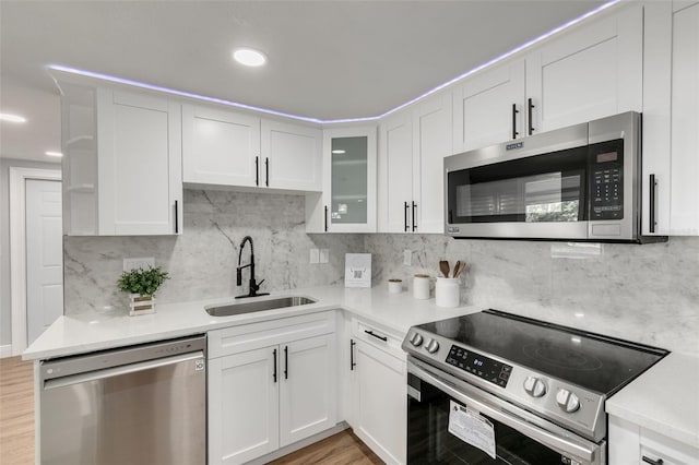 kitchen featuring appliances with stainless steel finishes, light wood-type flooring, backsplash, sink, and white cabinetry