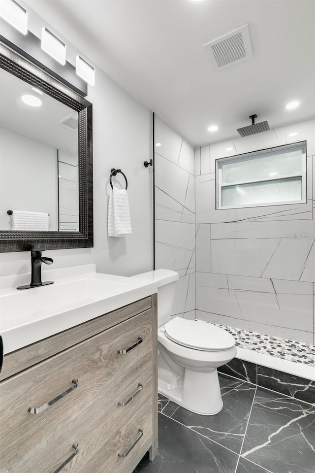 bathroom featuring a tile shower, vanity, and toilet