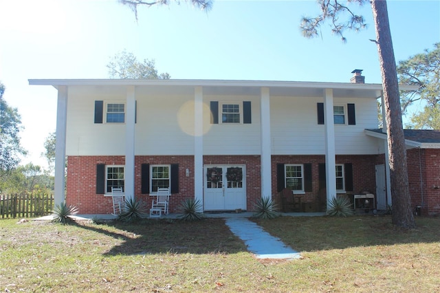 view of front facade with covered porch, brick siding, fence, a front lawn, and a chimney