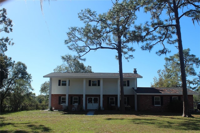 greek revival house with brick siding, a chimney, a front yard, and fence