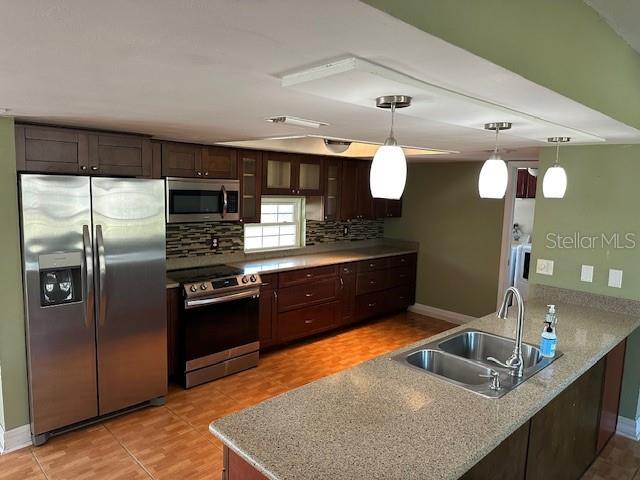 kitchen with a peninsula, dark brown cabinetry, stainless steel appliances, and a sink