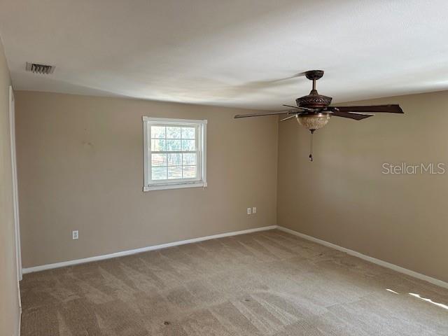 carpeted spare room featuring baseboards, visible vents, and ceiling fan