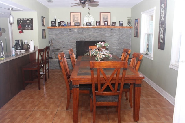 dining space with tile patterned flooring, baseboards, a ceiling fan, and a stone fireplace