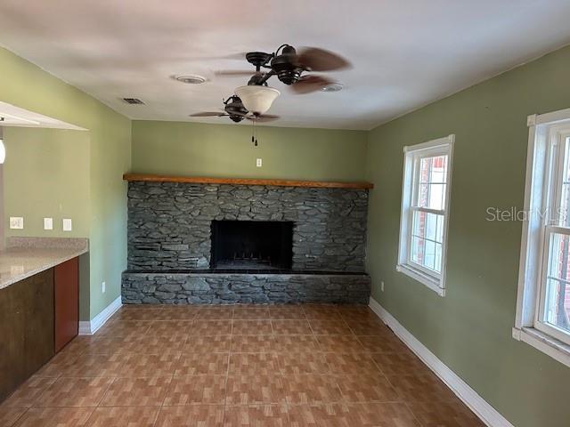 unfurnished living room featuring visible vents, a fireplace, a ceiling fan, and baseboards