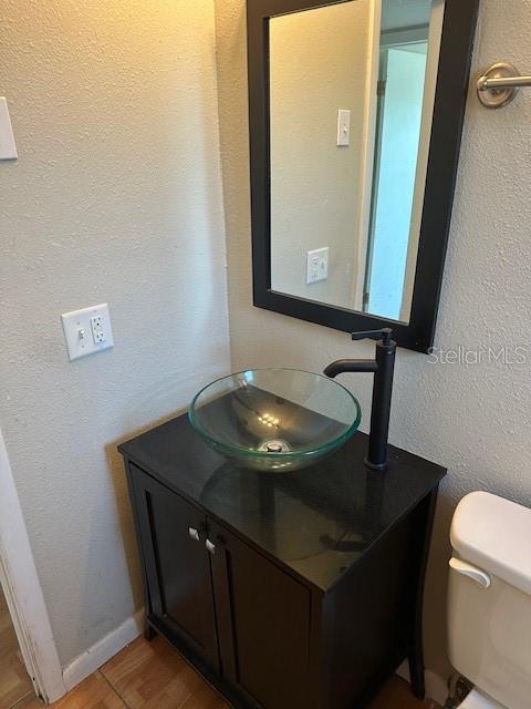 half bath with a textured wall, toilet, wood finished floors, vanity, and baseboards