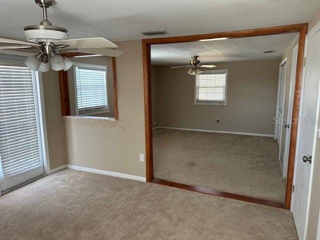 carpeted empty room with visible vents, ceiling fan, and baseboards