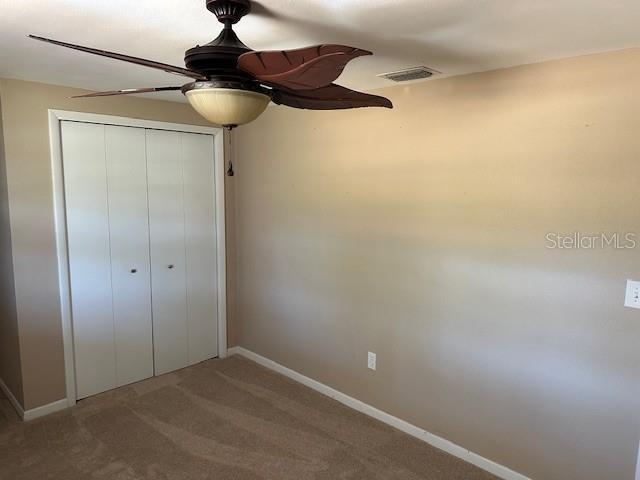 unfurnished bedroom featuring a ceiling fan, visible vents, baseboards, a closet, and carpet