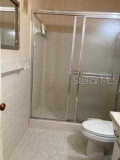 bathroom featuring tile patterned flooring, a shower with door, vanity, and toilet