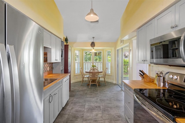 kitchen featuring butcher block countertops, hanging light fixtures, stainless steel appliances, and vaulted ceiling