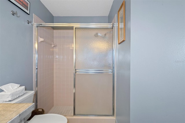 bathroom with a textured ceiling, an enclosed shower, and toilet