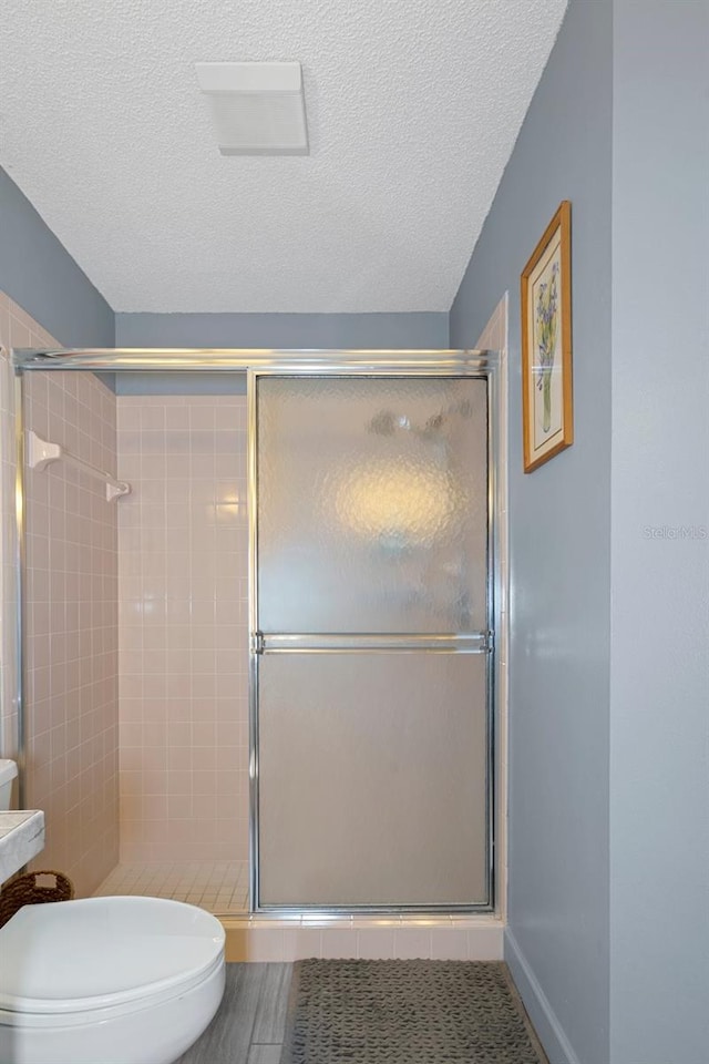 bathroom featuring a shower with shower door, a textured ceiling, and toilet