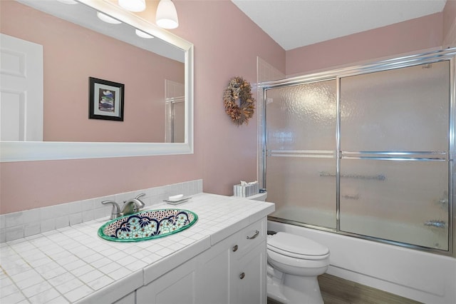 full bathroom with hardwood / wood-style floors, vanity, toilet, and bath / shower combo with glass door