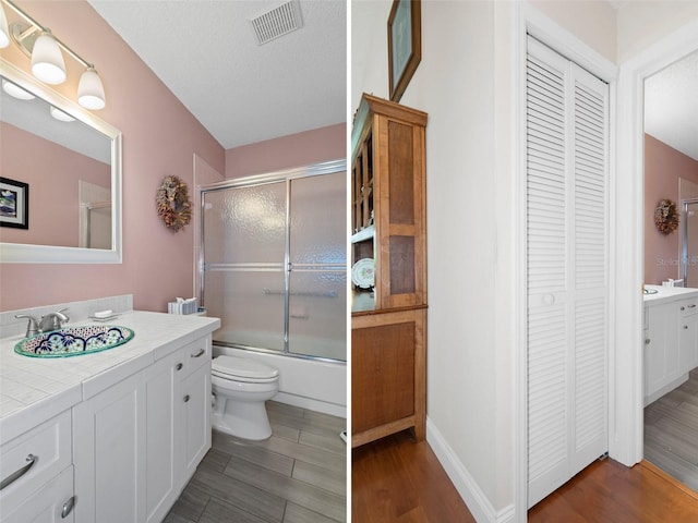 full bathroom with a textured ceiling, vanity, hardwood / wood-style flooring, enclosed tub / shower combo, and toilet