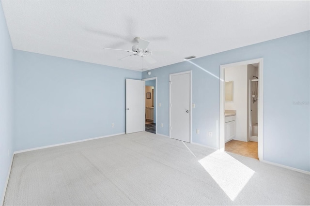 unfurnished bedroom with a closet, connected bathroom, light colored carpet, and ceiling fan