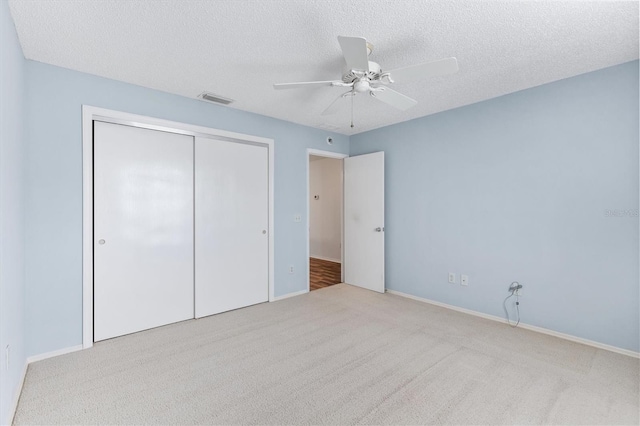 unfurnished bedroom featuring ceiling fan, light colored carpet, a textured ceiling, and a closet