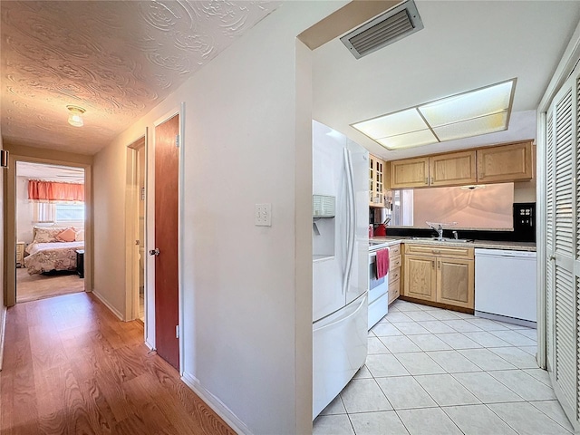 kitchen featuring light wood-type flooring, a textured ceiling, white appliances, and sink