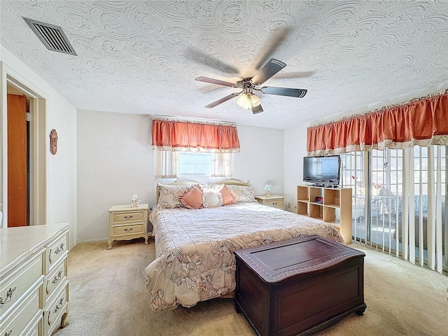 bedroom with ceiling fan, light colored carpet, and a textured ceiling