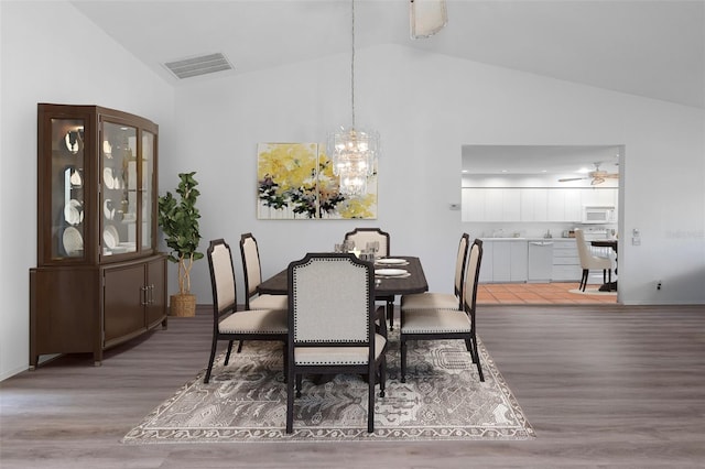 dining room featuring hardwood / wood-style flooring, ceiling fan with notable chandelier, and vaulted ceiling