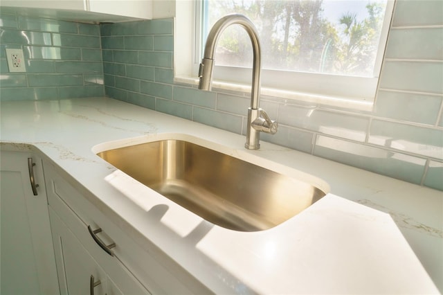 room details featuring white cabinets, tasteful backsplash, light stone counters, and sink