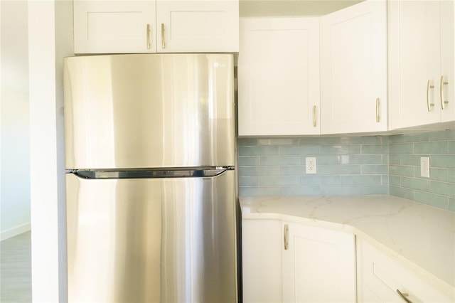 kitchen with white cabinets, light stone countertops, tasteful backsplash, wood-type flooring, and stainless steel refrigerator