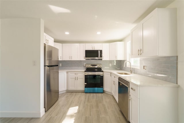 kitchen with light stone countertops, stainless steel appliances, sink, white cabinets, and light hardwood / wood-style floors