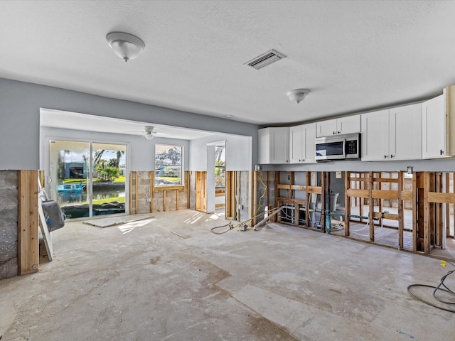 interior space with white cabinets, a textured ceiling, ceiling fan, and wood walls