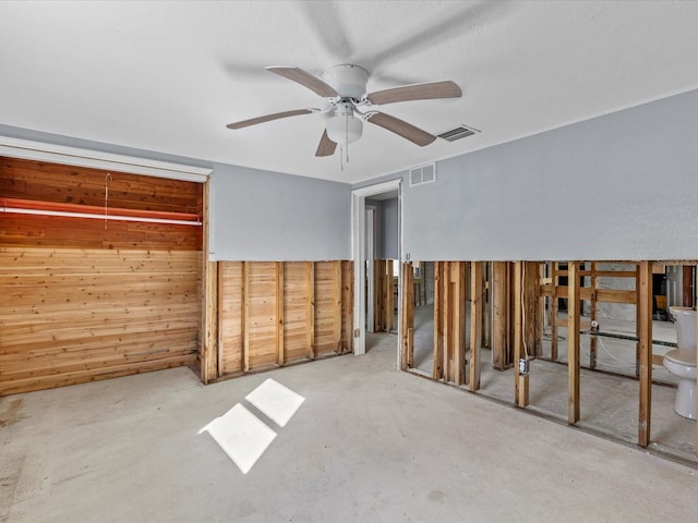 empty room with wooden walls, ceiling fan, and concrete floors