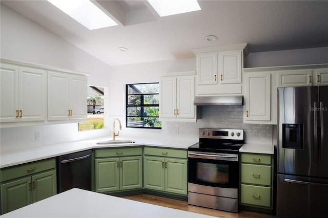 kitchen with stainless steel appliances, lofted ceiling with skylight, exhaust hood, sink, and white cabinets