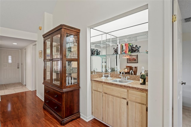 bar featuring wood-type flooring, a textured ceiling, light brown cabinetry, and sink