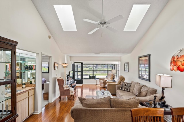 living room featuring a skylight, ceiling fan, high vaulted ceiling, and light wood-type flooring