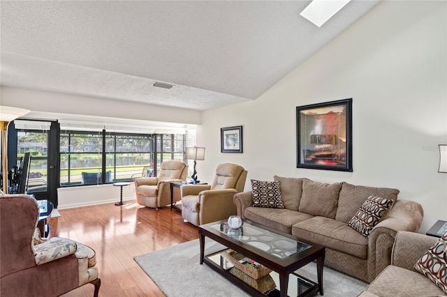 living room with vaulted ceiling with skylight, a healthy amount of sunlight, a textured ceiling, and light hardwood / wood-style flooring