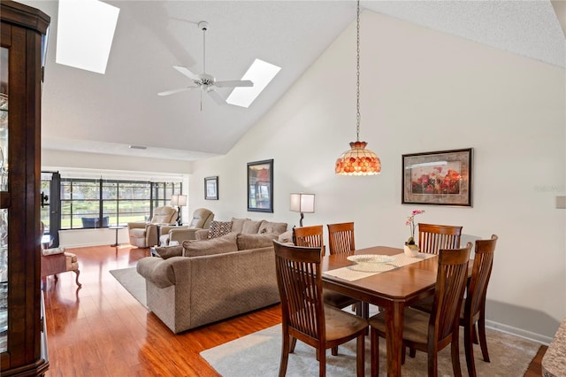 dining area with light wood-type flooring, a skylight, high vaulted ceiling, and ceiling fan