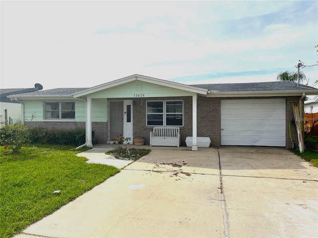 single story home with driveway, brick siding, an attached garage, covered porch, and a front yard