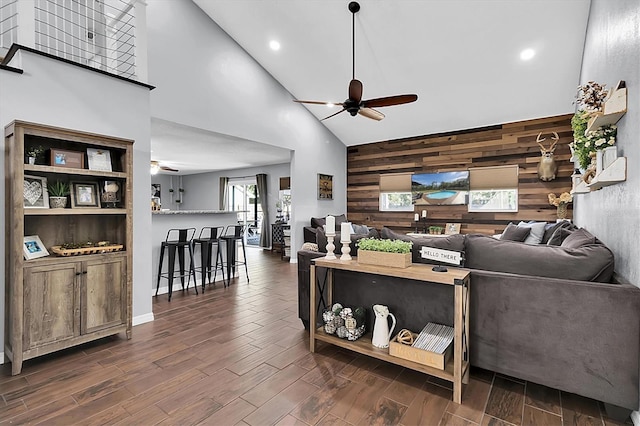 living room with wood walls, high vaulted ceiling, dark wood-type flooring, and ceiling fan