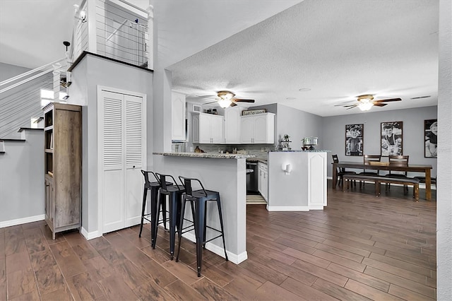 kitchen featuring dark wood-type flooring, white cabinets, a kitchen breakfast bar, a textured ceiling, and kitchen peninsula