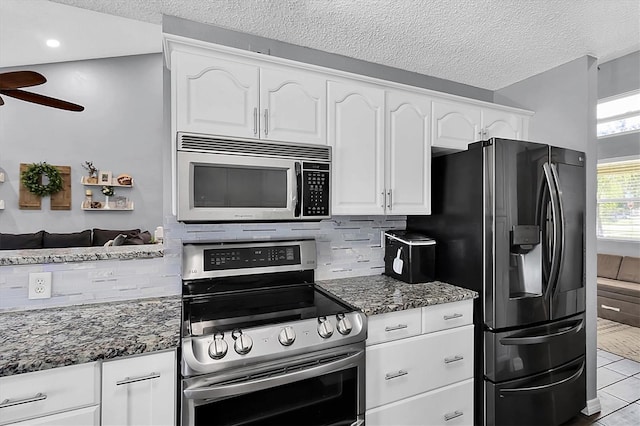 kitchen featuring light tile patterned floors, tasteful backsplash, dark stone counters, white cabinets, and appliances with stainless steel finishes