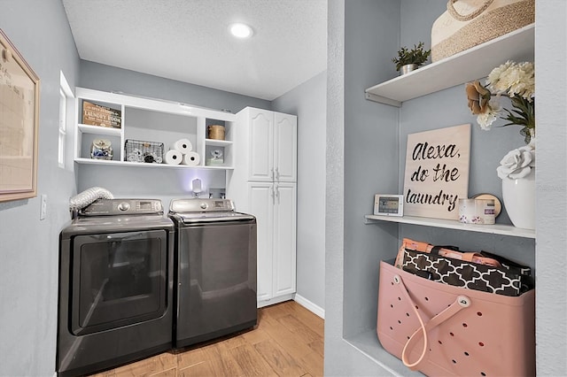 laundry room with washer and clothes dryer, cabinets, light wood-type flooring, and a textured ceiling