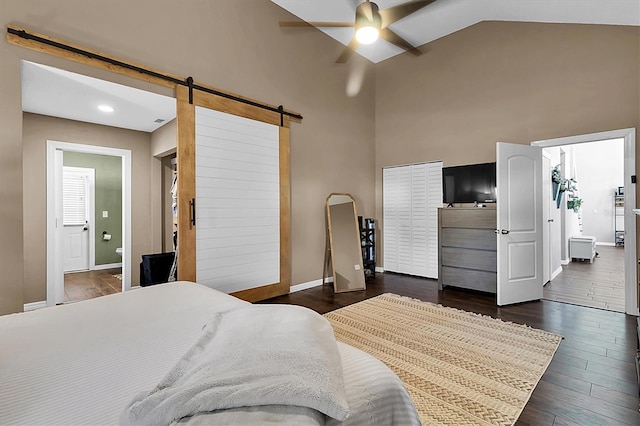 bedroom with a barn door, ceiling fan, dark hardwood / wood-style flooring, and high vaulted ceiling