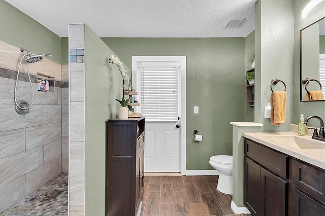 bathroom with a tile shower, vanity, a textured ceiling, and toilet