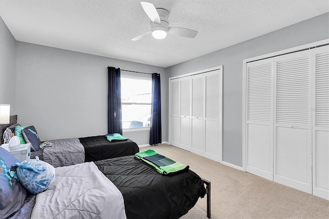 carpeted bedroom with ceiling fan, a textured ceiling, and two closets