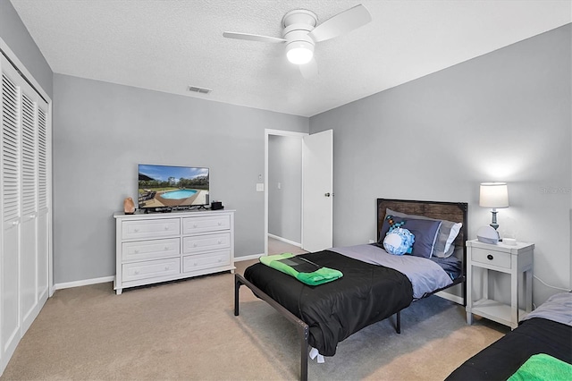 bedroom with ceiling fan, light colored carpet, a textured ceiling, and a closet