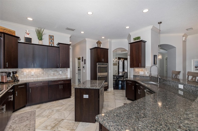 kitchen featuring dark stone counters, sink, decorative light fixtures, a kitchen island, and stainless steel double oven