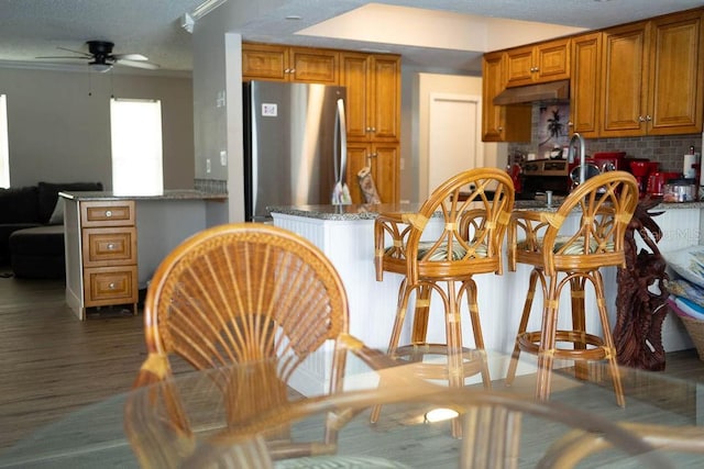 kitchen with dark hardwood / wood-style floors, ceiling fan, tasteful backsplash, kitchen peninsula, and stainless steel refrigerator