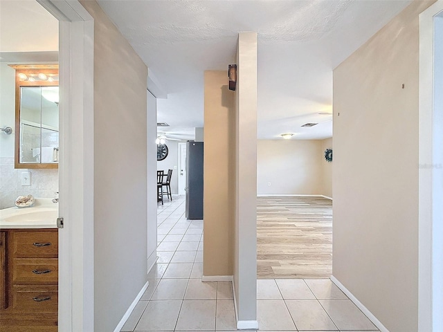 corridor featuring a textured ceiling, light tile patterned floors, and sink