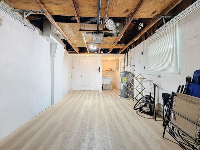 basement featuring electric water heater, sink, and light hardwood / wood-style floors